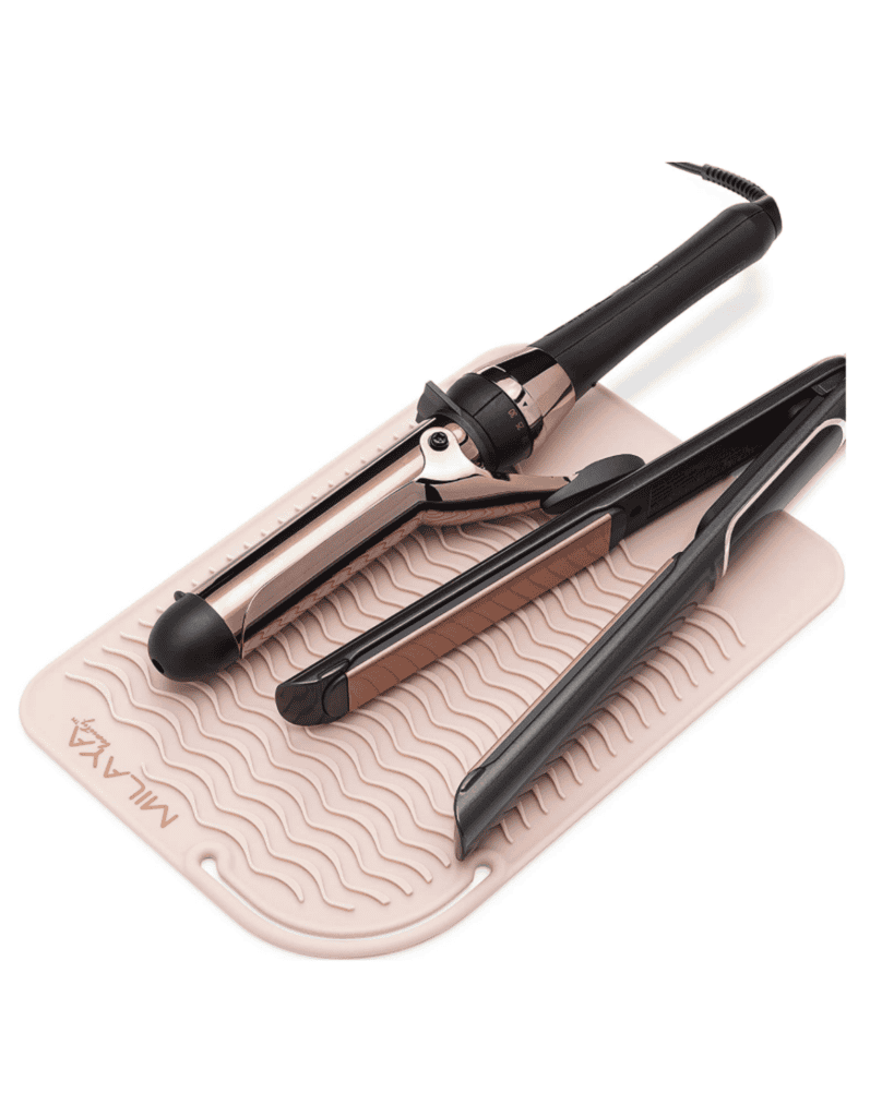 A curling iron and hair straightener, essential beauty tools, rest on a textured, wavy light pink heat-resistant mat. The tools feature sleek black and rose gold details.