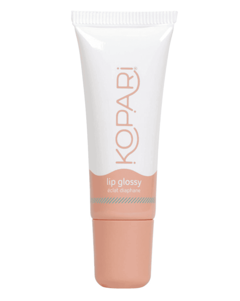 A white and peach-colored tube labeled "Kopari Lip Glossy" with "éclat diaphane" underneath sits among your beauty essentials. The packaging is sleek and sophisticated, featuring a handy screw-on cap.