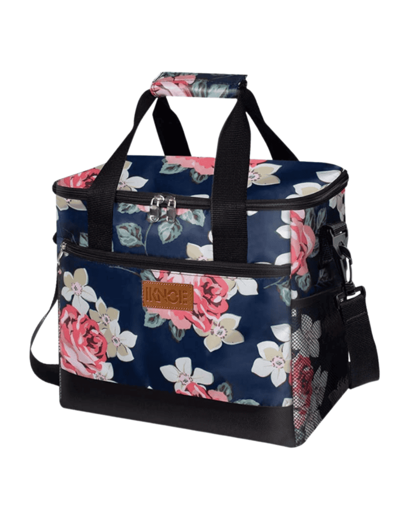 This floral-patterned cooler bag, perfect as travel gear for kids, showcases pink and white flowers on a dark backdrop. It features black handles, a detachable shoulder strap, and a front pocket with a brown label. The bag includes a zippered top and side mesh pocket for convenience.