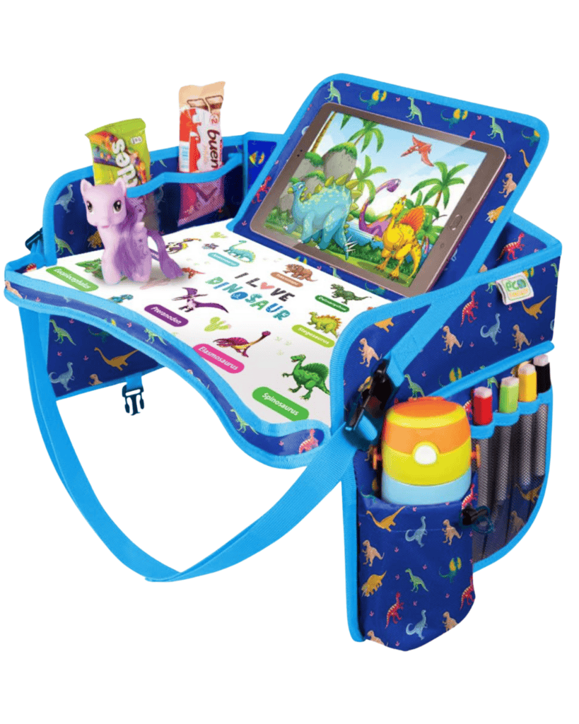 A colorful travel tray, essential travel gear for kids, showcases dinosaur designs with an iPad displaying a dinosaur game. It holds a purple toy horse, snacks, and a cup. The tray includes pockets for colored markers and features a strap for easy carrying.