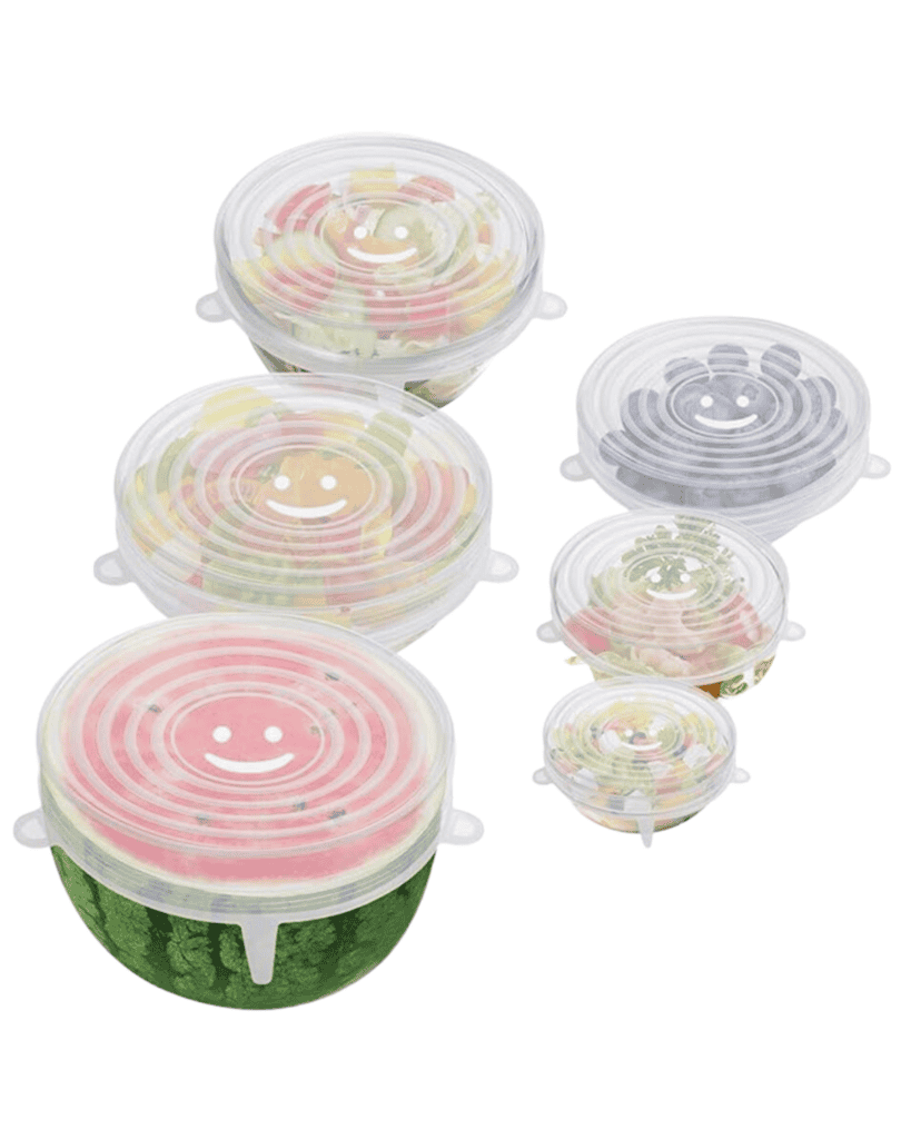 A set of seven transparent silicone stretch lids serves as eco-friendly containers for various sizes of bowls carrying fruits and vegetables. These lids boast ribbed tabs for easy removal, providing a snug fit over a watermelon, salad, and other food items.