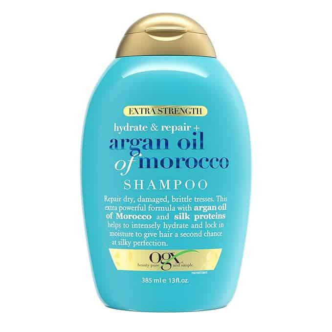 A blue bottle of OGX Hydrate & Repair Extra Strength Argan Oil of Morocco Shampoo with a gold cap, featuring text on the benefits of argan oil and silk proteins for dry, damaged hair. Capacity: 385 ml (13 fl oz). Look for exclusive Wednesday Deals to rejuvenate your hair routine.