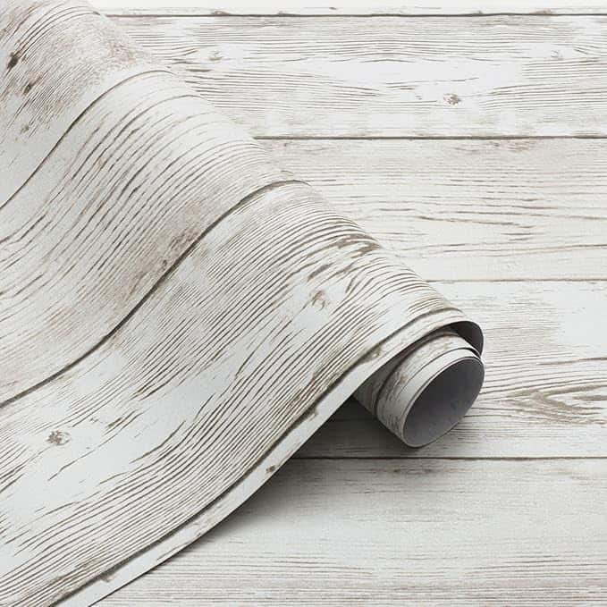 A roll of wood-patterned wallpaper, partially unrolled on a matching wooden surface, features a light, rustic texture and grain design—perfect for sprucing up your space with this week's exclusive Wednesday Deals.