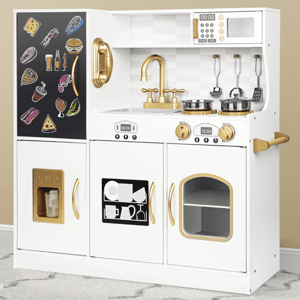 A children's play kitchen with a black refrigerator adorned in colorful food magnets is part of our Tuesday Deals. It features a white stove with gold handles, a sink with a gold faucet, an oven, microwave, and utensils hanging above. The set rests on a gray carpet.