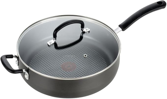 This black non-stick frying pan, perfect for Friday Deals, comes with a glass lid. It features a long handle and a shorter loop handle. The textured surface inside boasts a circular patterned center, while the lid is topped with a sleek black handle.