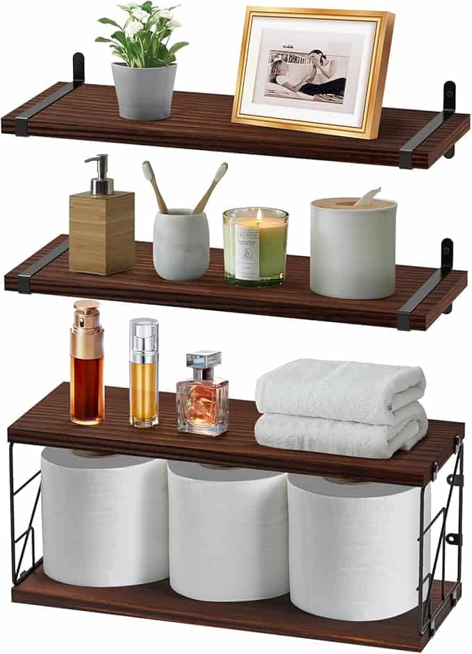 Three wooden wall-mounted shelves are displayed. The top shelf showcases a plant and a framed photo. The middle holds toiletries and candles, perfect for sprucing up your space with Friday Deals in mind. The bottom features three rolls of toilet paper, folded towels, and perfume bottles.