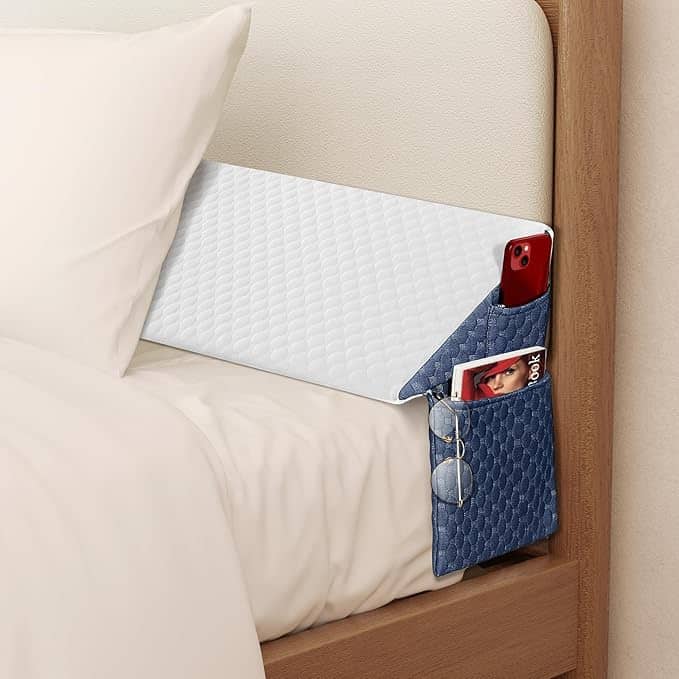 Score big with our Friday Deals on a white headboard pocket organizer. Perfect for your essentials, it holds a red phone, glasses, and a magazine. The quilted blue pocket beautifully contrasts with the wooden bed frame and crisp white bedding.