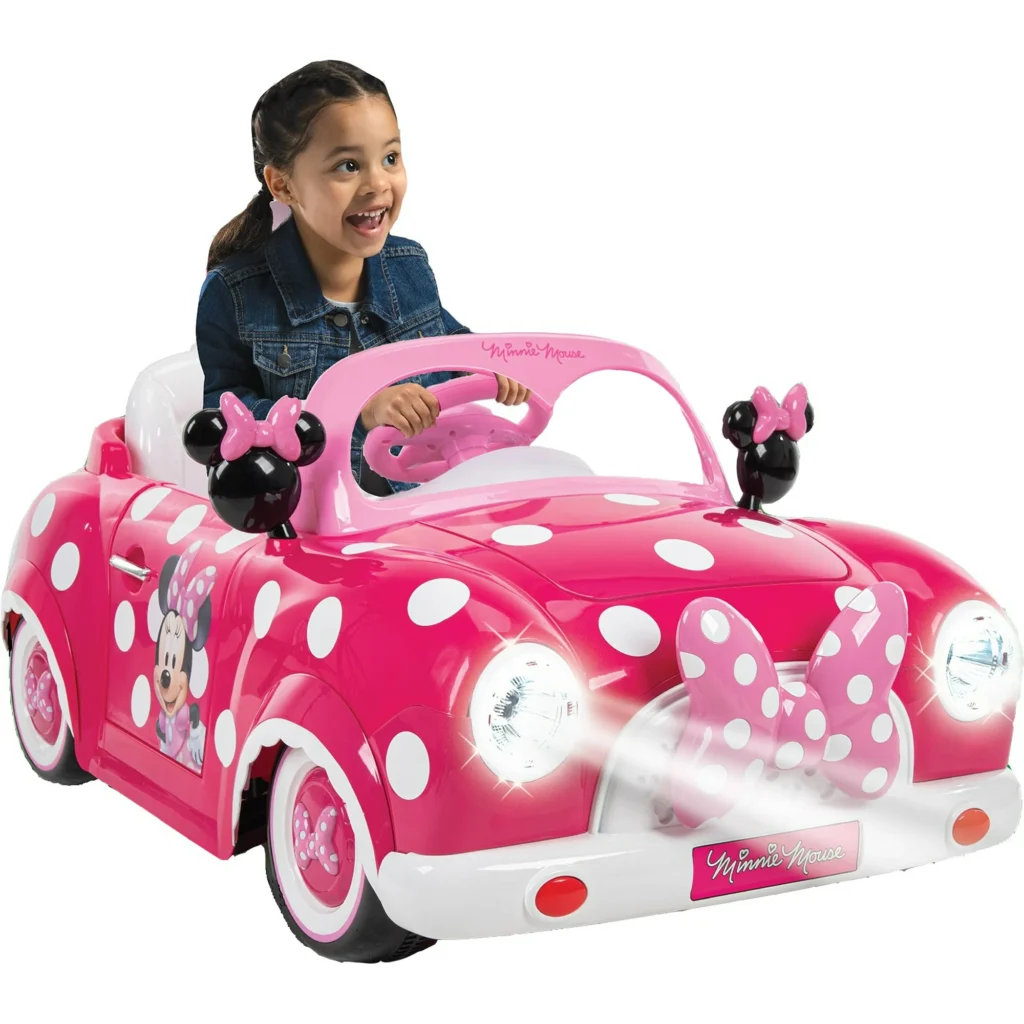 A child sits in a pink toy car with white polka dots, themed after Minnie Mouse. The car features Minnie's bow and ears on the front. The child is smiling, enjoying the ride—a perfect moment to capture during our exciting Friday Deals!