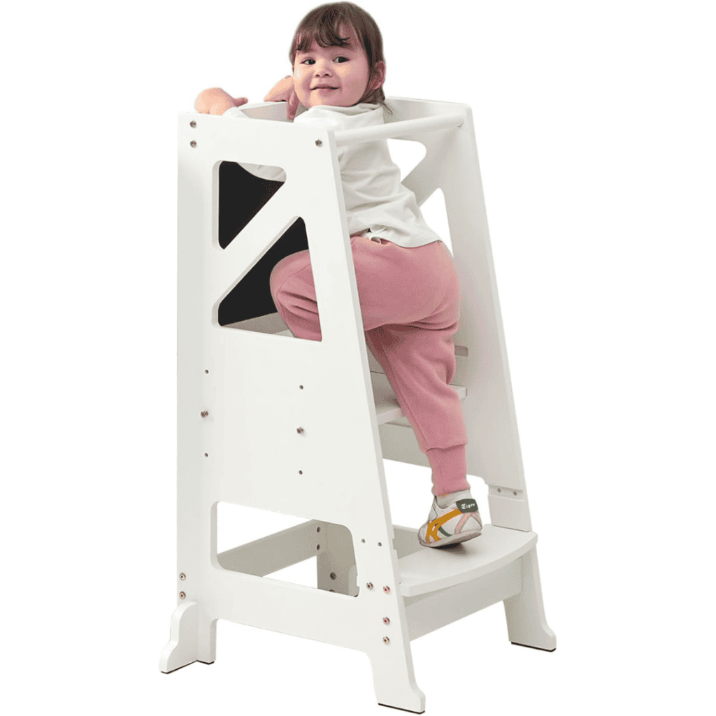 A small child is climbing a white step stool during Friday Deals. The child is wearing a white shirt and pink pants with patterned shoes. The step stool features side panels with cut-out handles for safety, set against a plain white background.