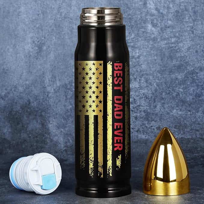 A black travel mug with "BEST DAD EVER" printed in red alongside a distressed American flag design sits on a textured gray background. The open cap and bullet-shaped gold lid rest beside it, available at an unbeatable price during Tuesday Deals.