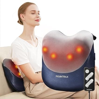 A woman sits with her eyes closed, enjoying a Mountrax back massager. The device emits soothing heat spots. She lounges on a beige couch in a white shirt and beige pants, remote control nearby, reveling in the relaxation offered by Friday Deals.