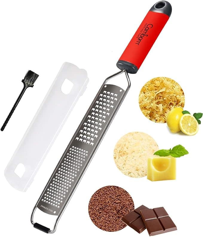 A food grater with a red handle, protective cover, and cleaning brush offers unbeatable Monday Deals. Featuring grated items like lemon, cheese, and chocolate in circles, its metal surface is designed with numerous small holes for efficient use.