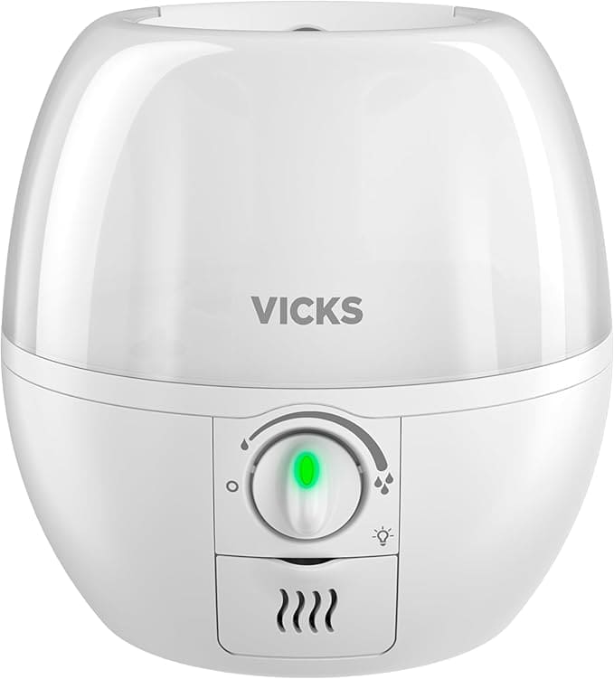 A white Vicks humidifier with a green power indicator is shown. The design is compact and round, featuring an adjustable knob for controlling mist output. Perfect for snagging on Wednesday Deals, this trusty appliance ensures comfort in every breath.