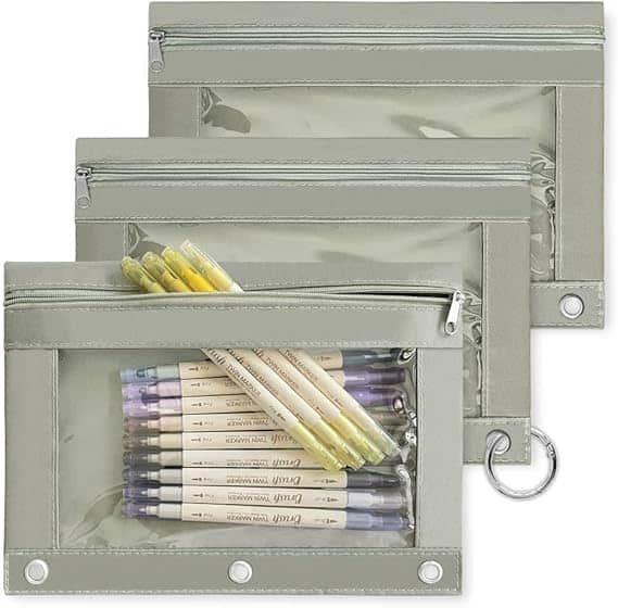 Three transparent pencil pouches with zippers are displayed, each brimming with pens and markers. With three-ring binder holes on the side, they effortlessly clip into any binder. Perfect for organizing essentials, these pouches are a steal during our Friday Deals!.