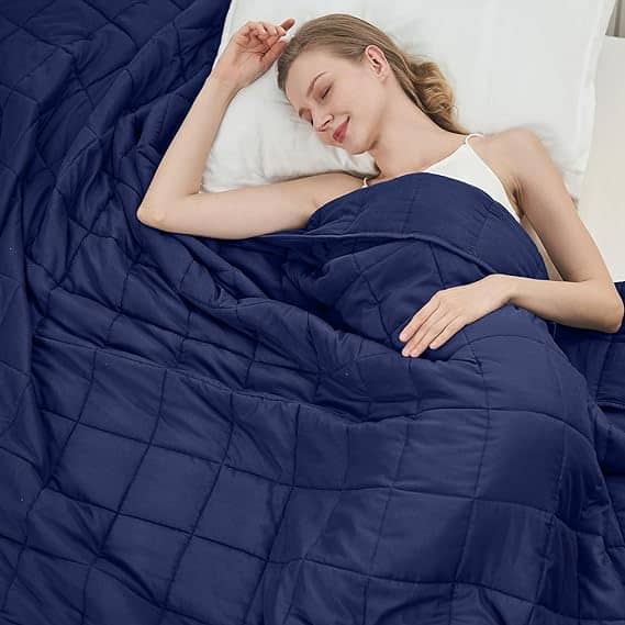 Amidst Friday Deals excitement, a woman peacefully sleeps on a white pillow, wrapped in a navy blue quilted blanket. She wears a white tank top, her hand resting gently on the blanket, with her head slightly tilted back in serene slumber.