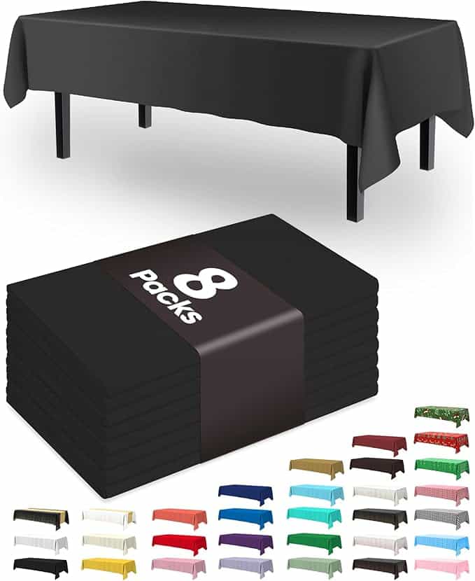 A black rectangular tablecloth is draped over a table, with a pack of eight folded black tablecloths in the foreground. A selection of various colored tablecloths is displayed at the bottom, perfect for spicing up your dining decor during Tuesday Deals.