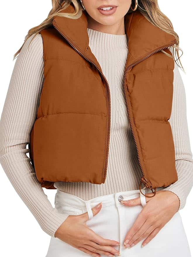 A person showcases a chic Friday Deals look with a brown puffer vest over a ribbed long-sleeve shirt and light-colored pants. The vest is zipped halfway, exuding casual elegance, as one hand rests in their pocket against the plain white background.