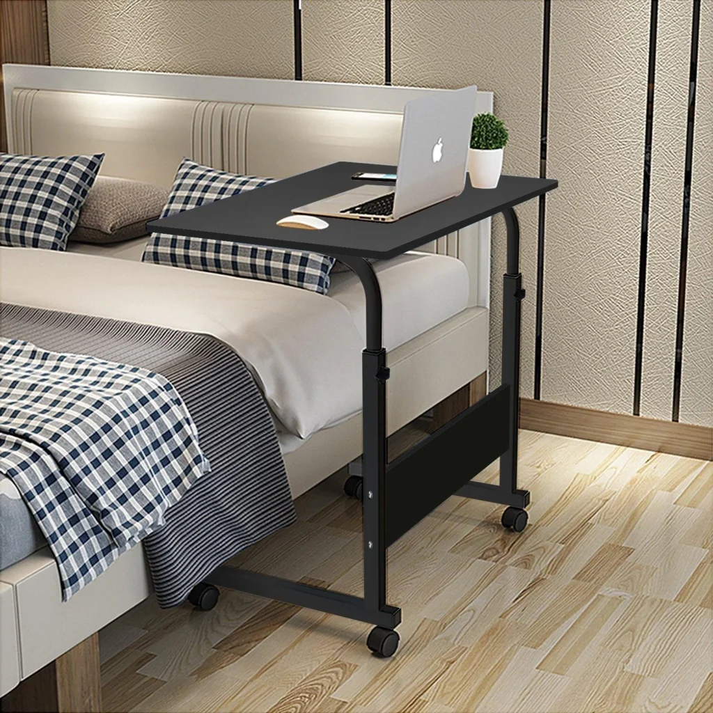 A modern bedroom showcases a bed with blue plaid pillows and a gray headboard. Beside it, an adjustable black rolling desk holds a laptop and a small plant, perfect for browsing Friday Deals. The room features light wood flooring and vertical striped wallpaper.