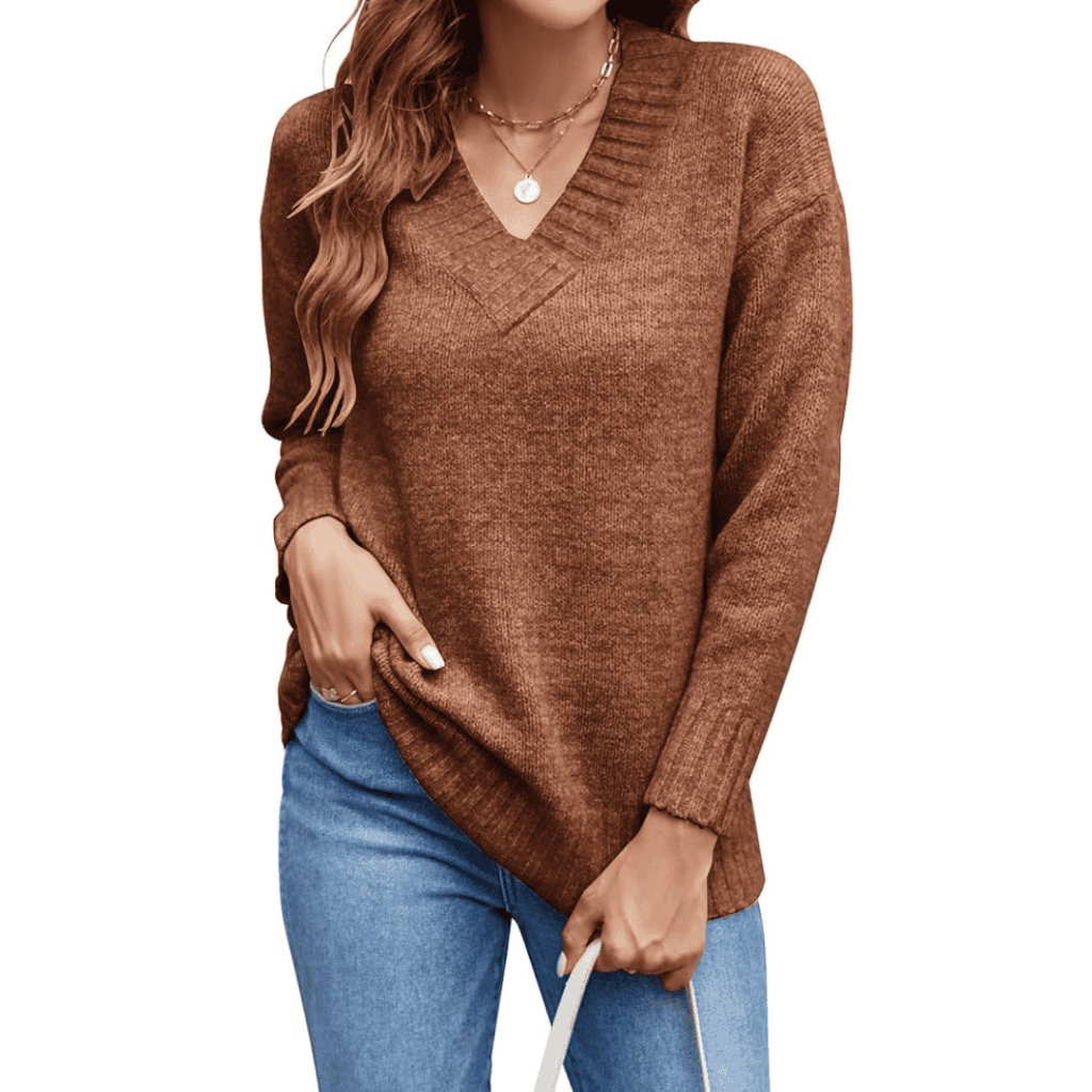 A person wearing a brown V-neck sweater, blue jeans, and a necklace showcases their long, wavy hair while holding a white bag—an effortlessly stylish look perfect for snagging Monday Deals in style.