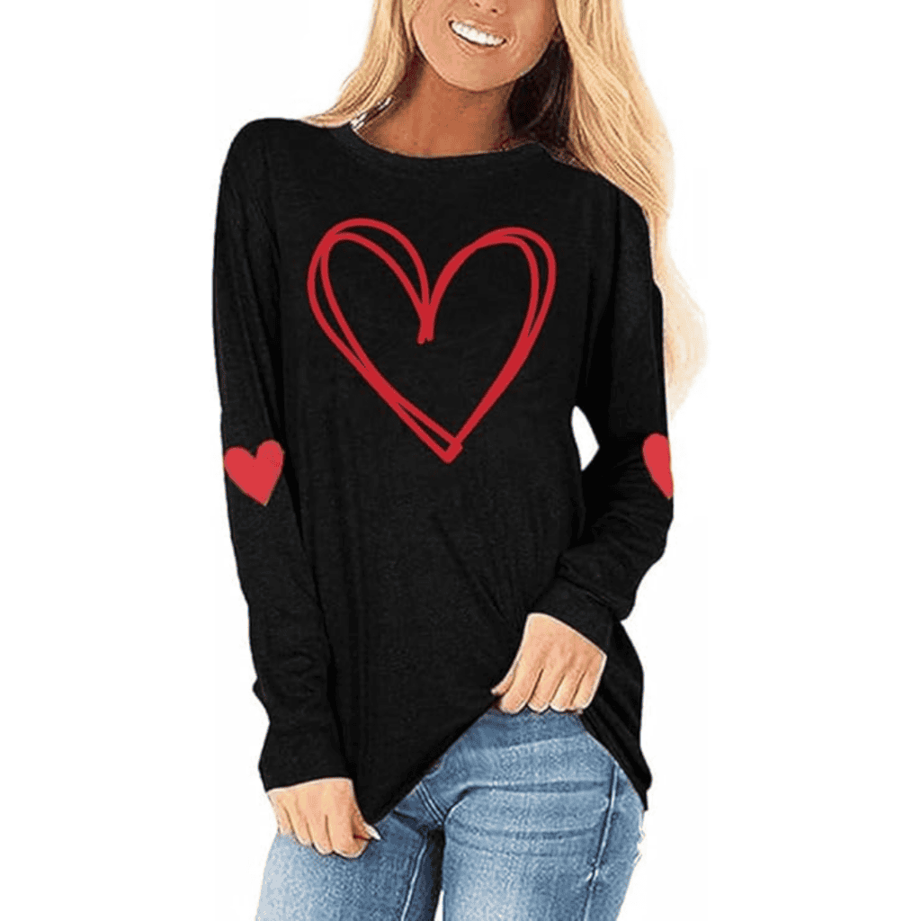 A woman, taking advantage of Tuesday Deals, wears a black long-sleeve shirt adorned with a striking red heart on the front and smaller hearts on the elbows. Her blonde hair cascades over her shoulders as she stands confidently in blue jeans, hand on hip.