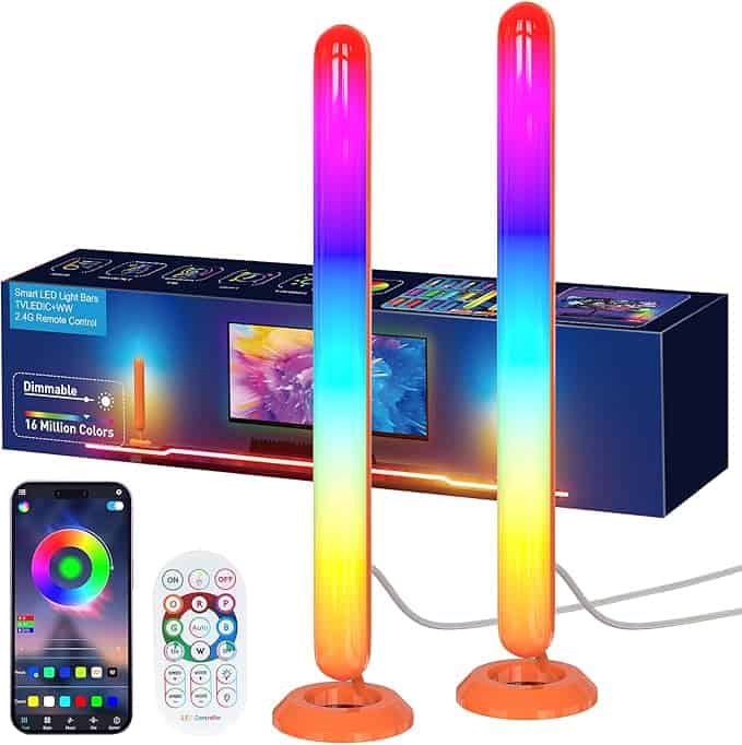 Two vertical LED light bars display a spectrum of colors, standing on round bases. Behind them, the box packaging showcases images of the lights. A smartphone and remote control offer color and brightness options, perfect for those irresistible Monday Deals.