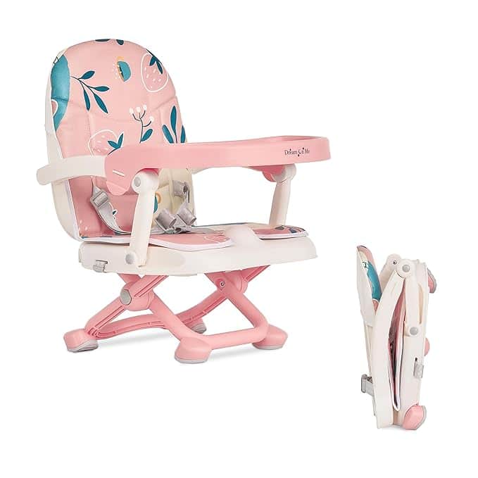 A pink and white foldable booster seat with floral patterns is shown in two positions: open and folded. Perfect for infants or toddlers, it features a safety harness and a tray. Don't miss out on this essential Monday Deals offer!.