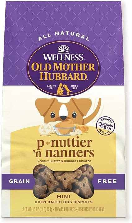 A purple and yellow bag of Old Mother Hubbard's P-Nuttier 'N Nanners dog biscuits, perfect for your furry friend. This grain-free treat features a cartoon dog savoring peanut butter and banana flavors, with visible biscuits through a clear window. Don't miss out on Wednesday Deals!.