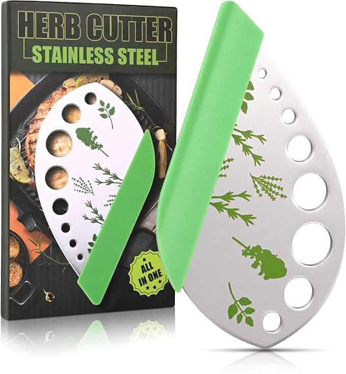 A stainless steel herb cutter with a green handle is showcased elegantly against its packaging box. Featuring leaf and herb patterns with circular cutouts, the packaging highlights an image of the cutter and culinary delights. Perfect for Monday Deals enthusiasts seeking kitchen essentials!.